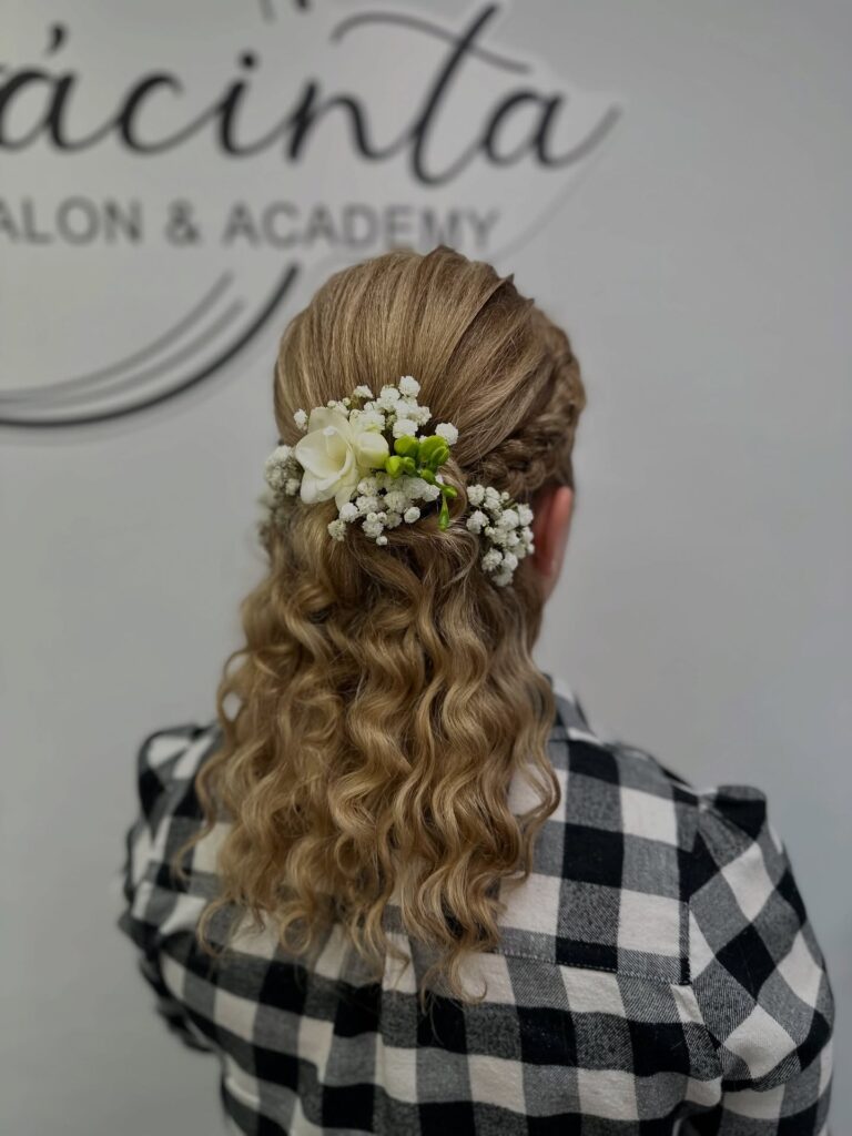 Golden blonde curly hair styled in a half up hairstyle with white floral accents.