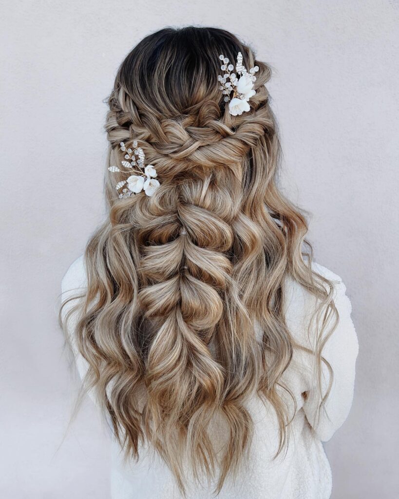 Long blonde wavy hair styled in a braided half up hairstyle with floral hair accessories.