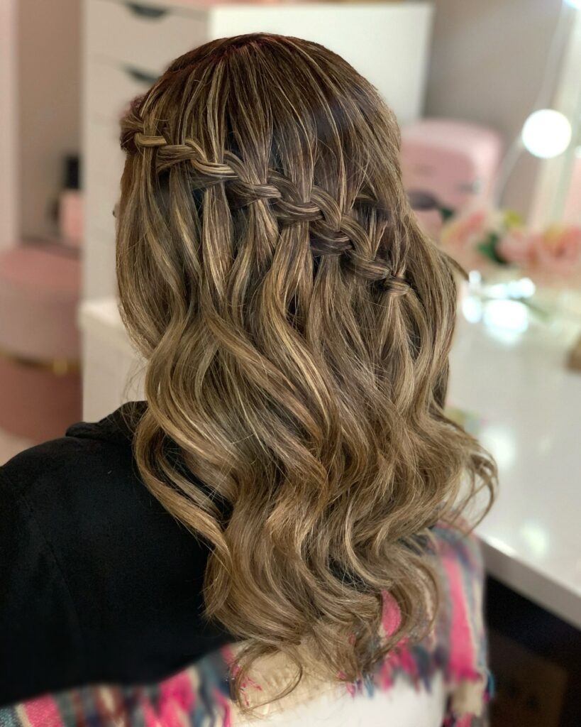 Medium length brunette hair with soft waves styled in a loose waterfall braid half up hairstyle.