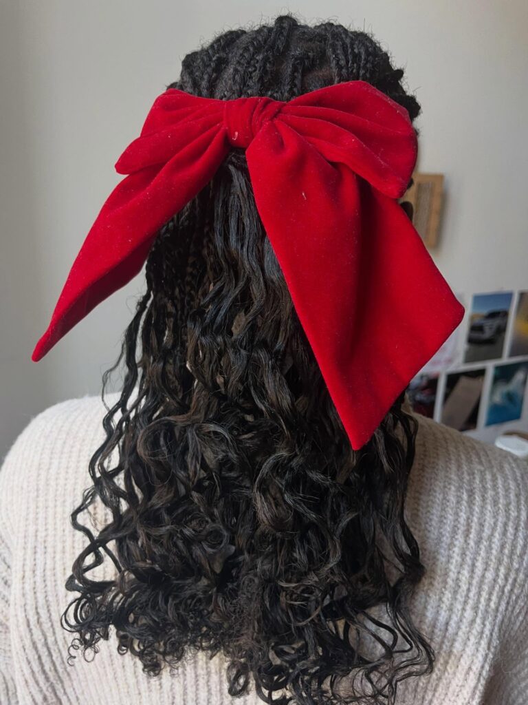 Half up braided hairstyle with loose curls and a large red bow tied at the back.