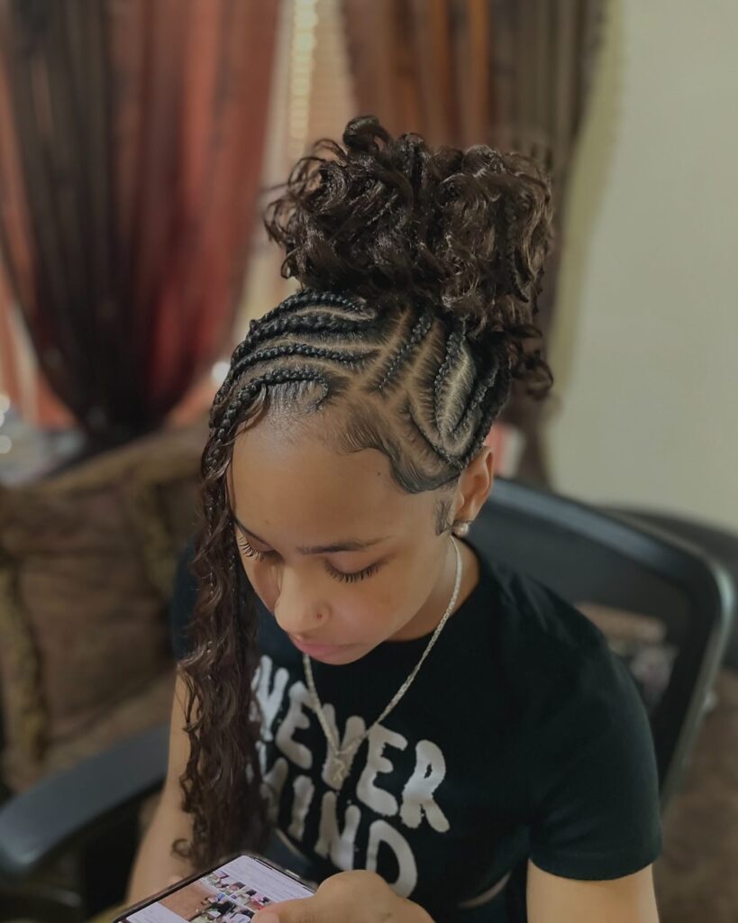 Swirled cornrow design styled into a high curly bun with one braid hanging at the side.