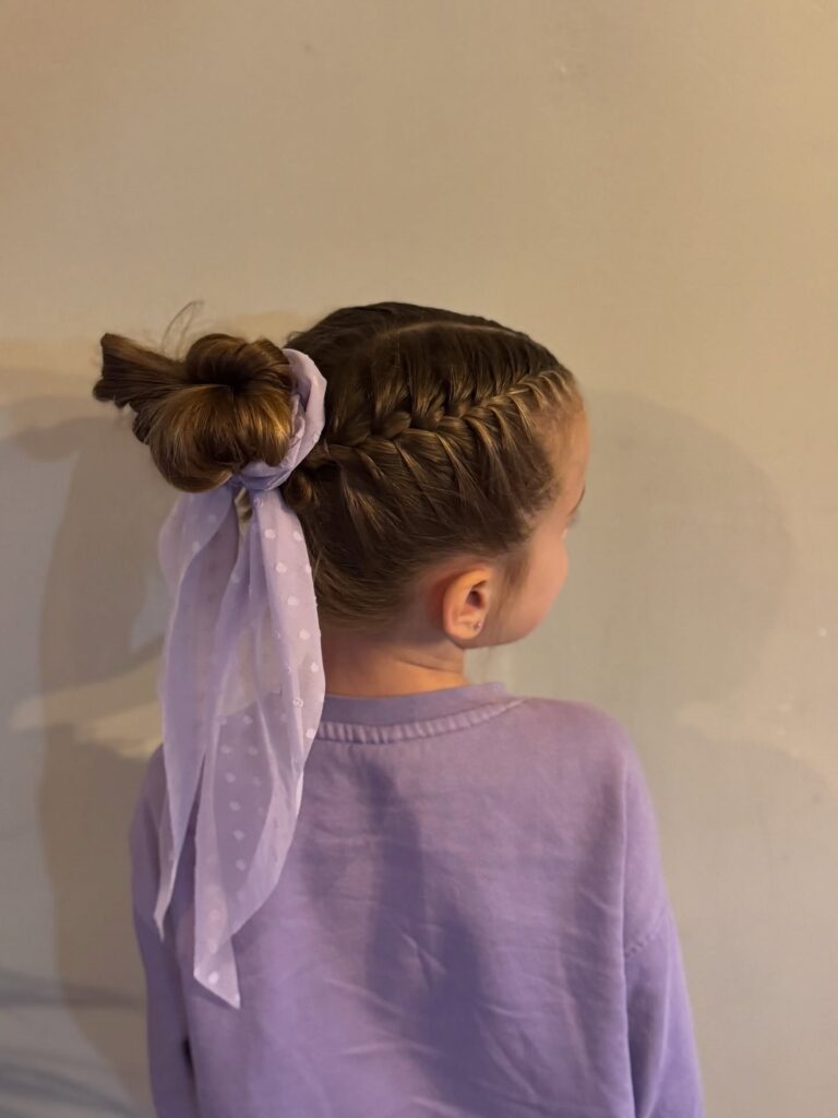 Braided hairstyle with side braids leading into a bun tied with a soft ribbon.