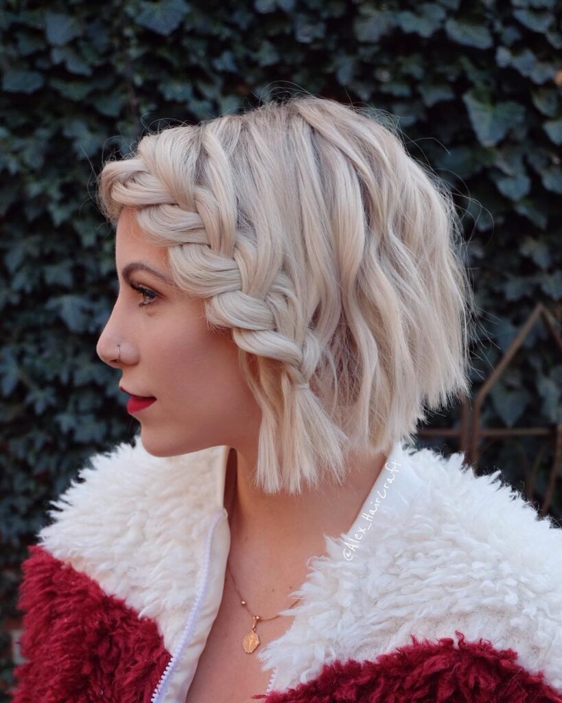 Short blonde bob with a thick side braid along the front and soft wavy texture.