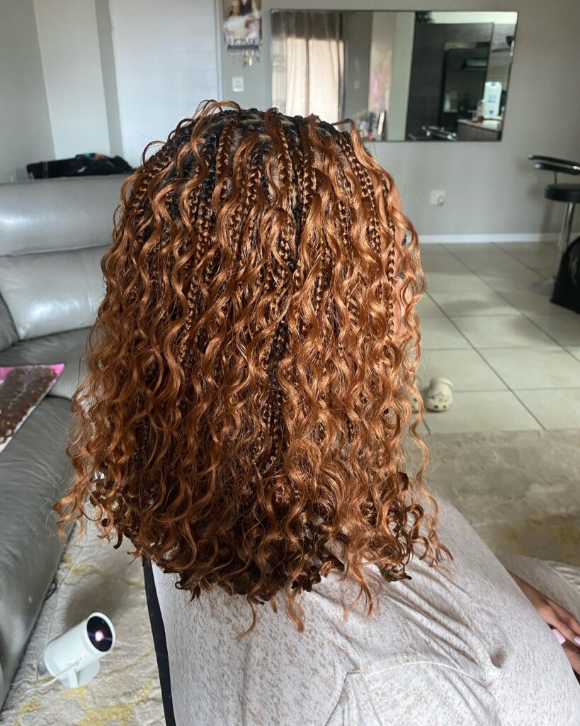 Short layered hairstyle with micro braids at the roots and voluminous curly ends in a warm copper shade.