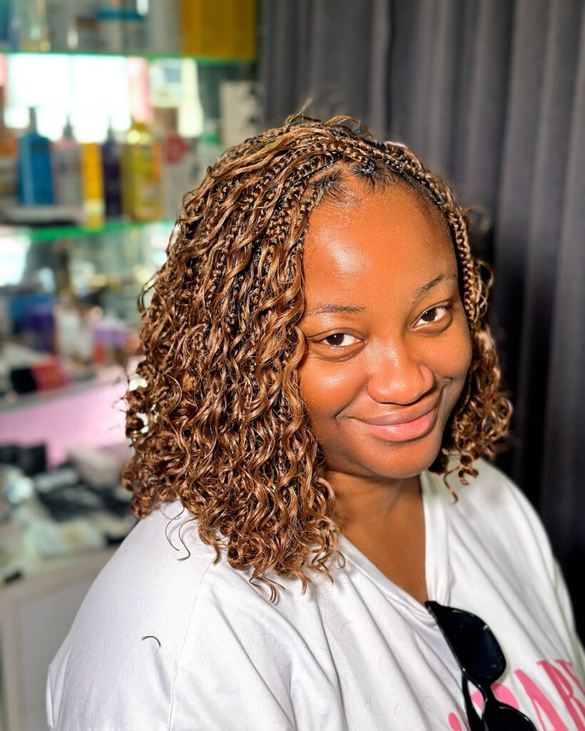 Short honey blonde micro braids with soft curly texture throughout.