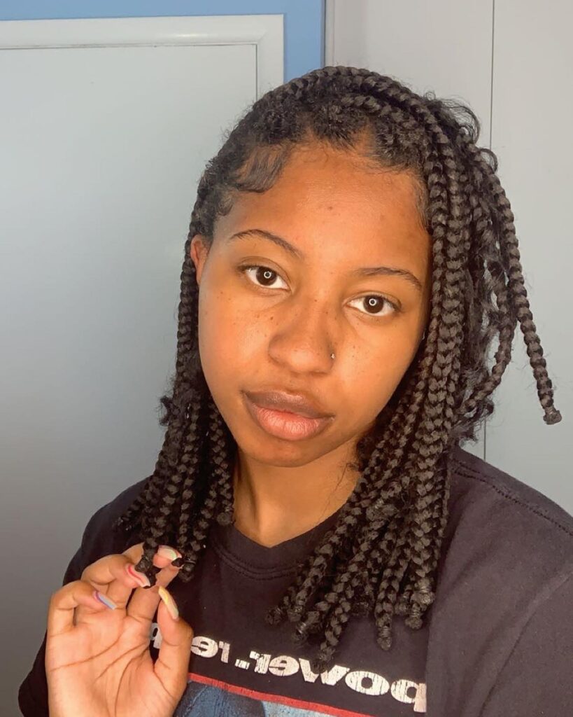 Short box braids with a side part and natural finish around the face.