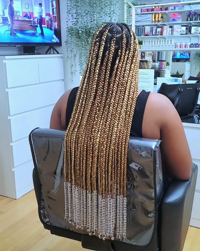 Long honey blonde box braids with clear beads attached at the ends.