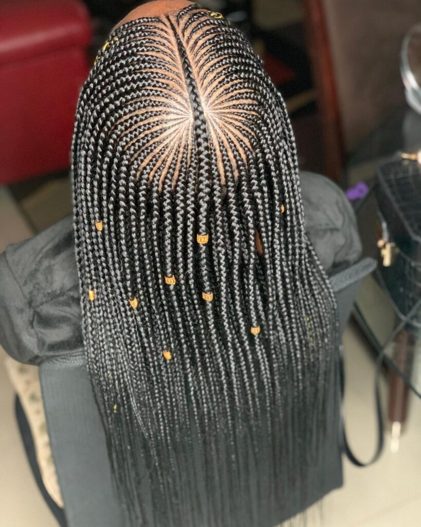 Long black box braids with a starburst scalp parting pattern and gold braid cuffs.