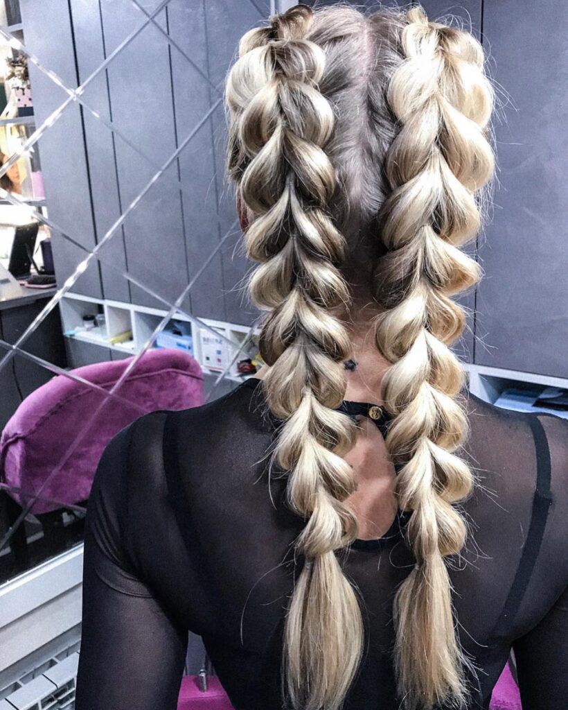 Blonde hair styled into two oversized bubble inspired Dutch braids.