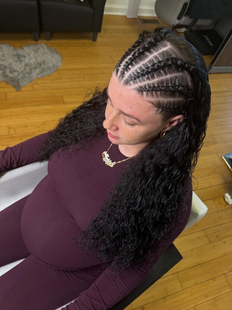 Curved scalp braids flow into long dark curly hair with a side swept braided design.