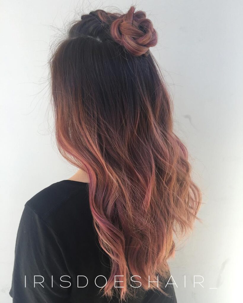 Long burgundy wavy hair styled in a half up bun with soft pink highlights.