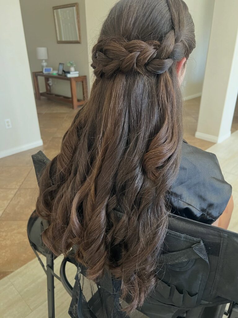 Long brunette curls styled in a half up hairstyle with twisted braided sections pinned at the back.
