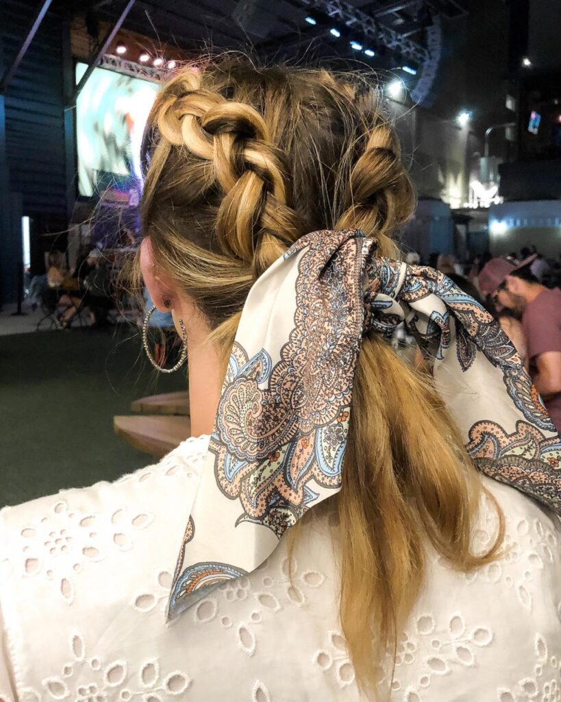 Blonde hair styled with chunky braids into a low ponytail tied with a patterned scarf.