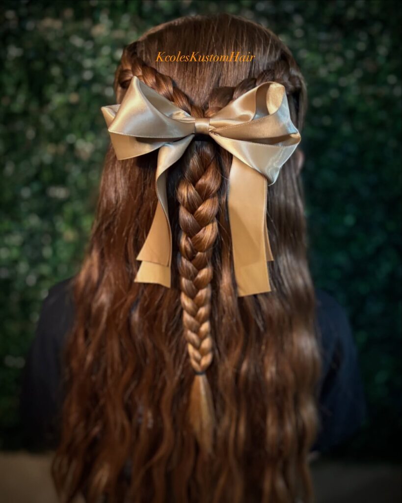 Long brunette hair styled with side braids, a center braid, and a large satin bow.