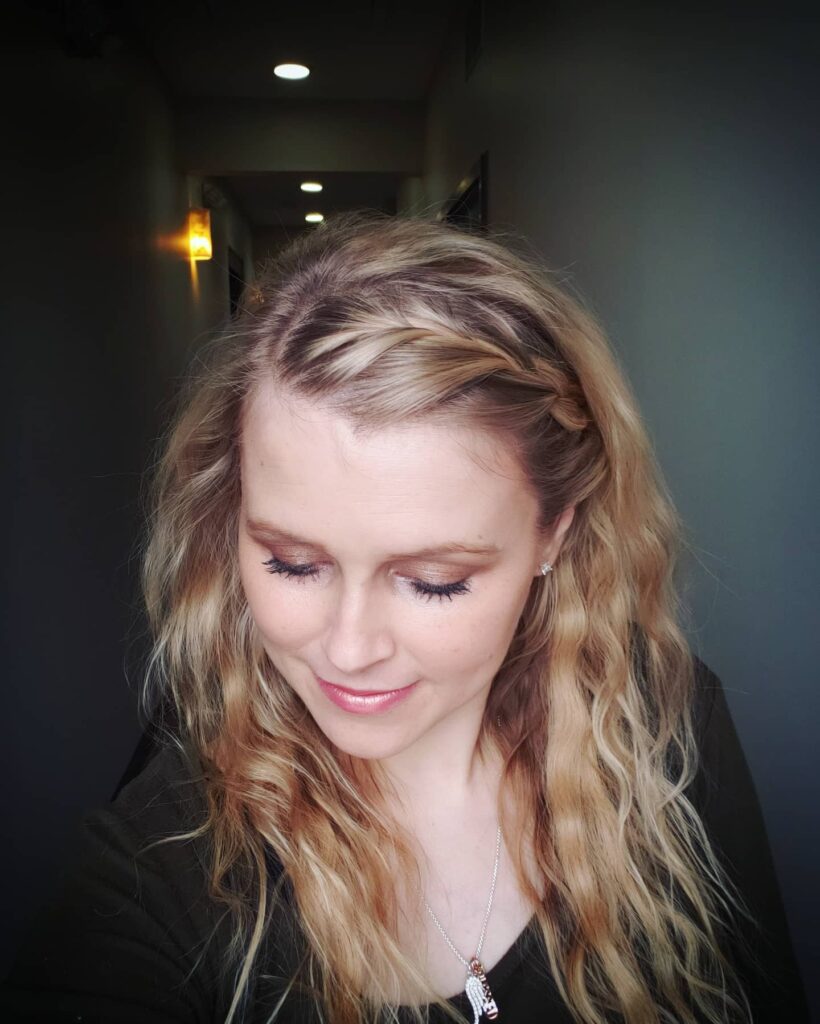 Loose blonde waves styled with a small braid along one side of the hair.