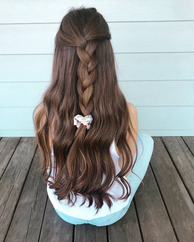 Long brunette wavy hair styled in a half up look with a chunky center braid.