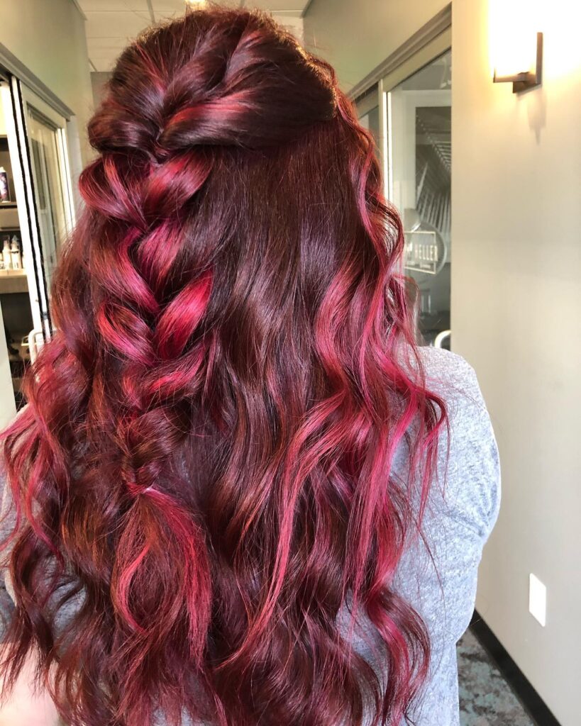 Long dark red wavy hair styled with a chunky side braid and bright magenta highlights.