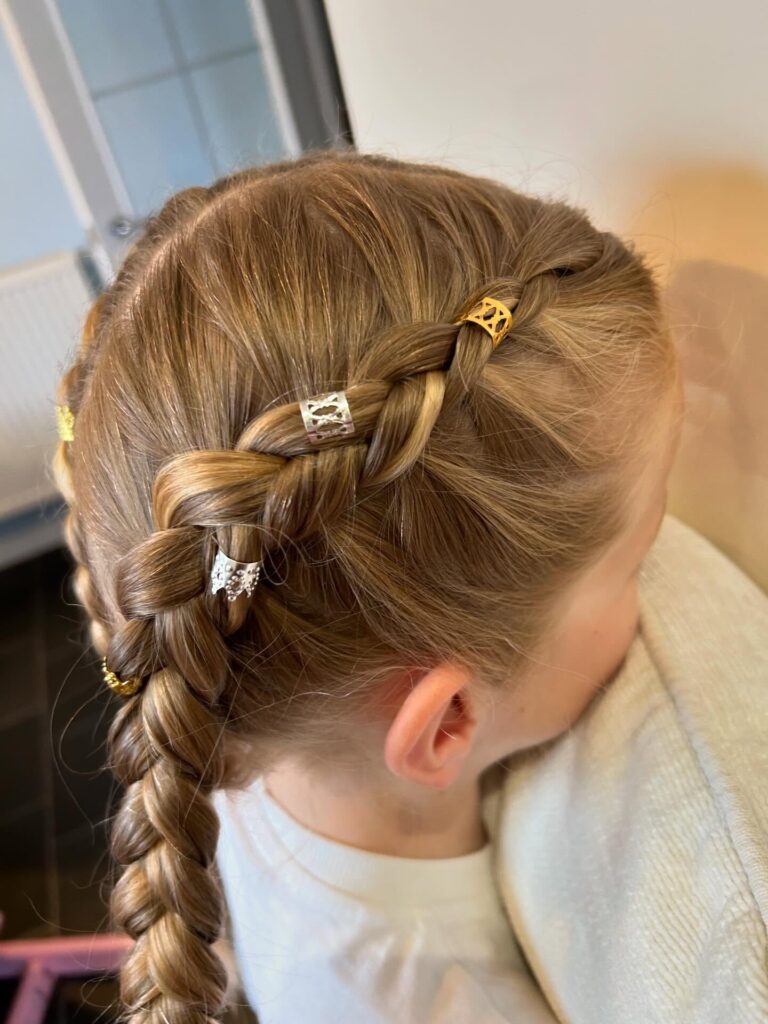 Blonde hair styled into chunky braided pigtails decorated with small metallic hair rings.
