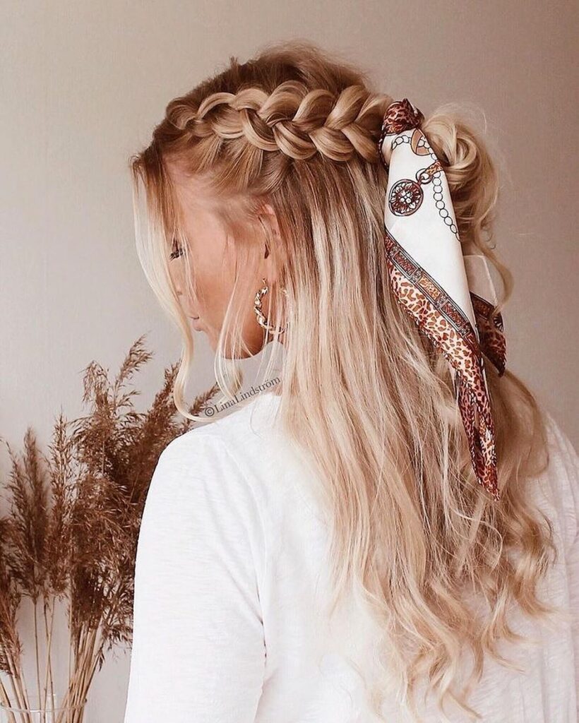 Blonde wavy hair styled with a side braid, messy half up bun, and printed scarf.