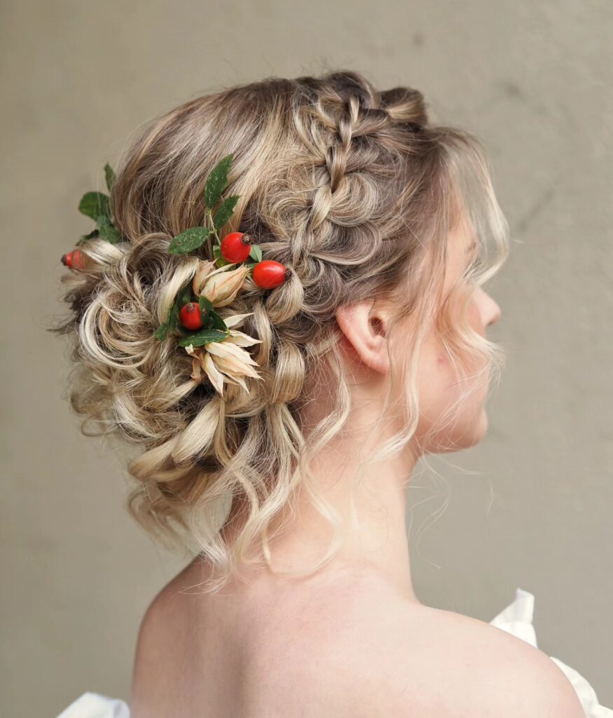 Loose blonde braided bun with floral accents and soft curled face framing strands.