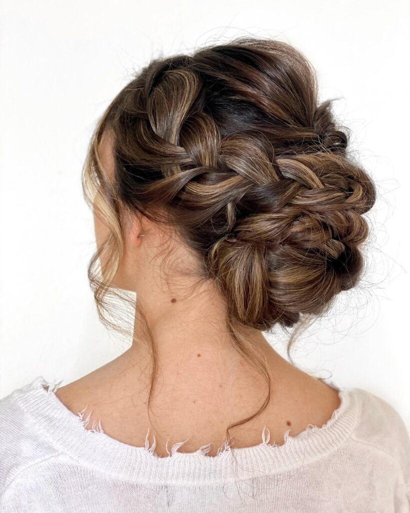 Soft brunette braided low bun with loose tendrils and woven texture at the back.