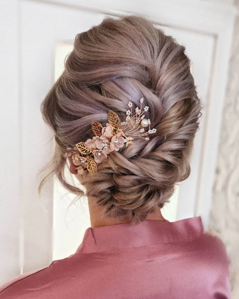 Textured braided twist updo with rosy blonde hair and floral gold hair accessory.