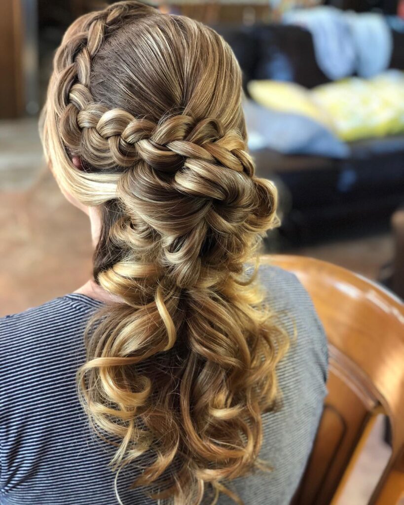 Half up braided hairstyle with loose brunette curls and highlighted waves.