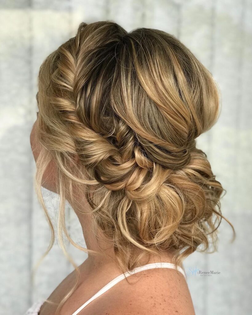 Voluminous blonde braided side bun with soft curls and textured twists.