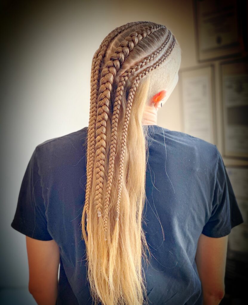 Side undercut hairstyle with tight cornrow braids blending into a long straight blonde ponytail.