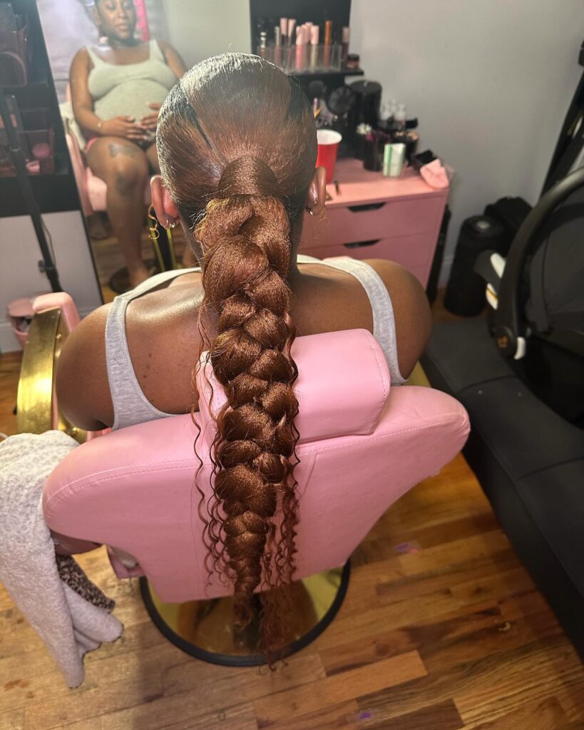 A copper brown braided bubble ponytail with loose curly ends and a sleek finish.
