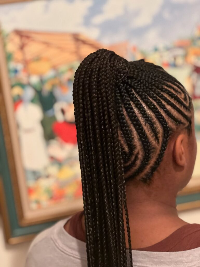 A high ponytail with long micro braids and curved braided parts.