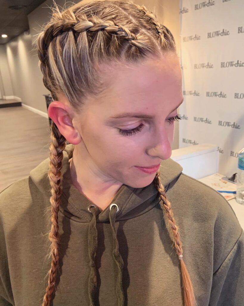 A woman with tight blonde boxer braids wearing a casual hoodie indoors.