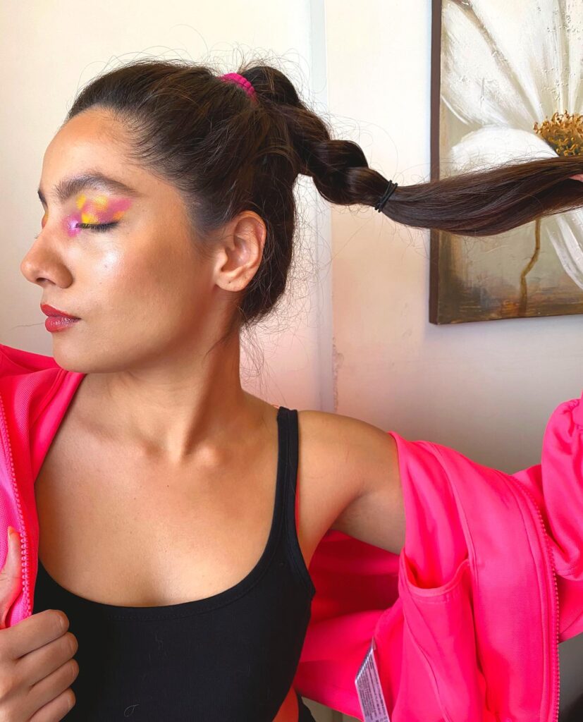 A woman wearing a sporty bubble ponytail with dark hair tied into sections and paired with bright pink workout styling.