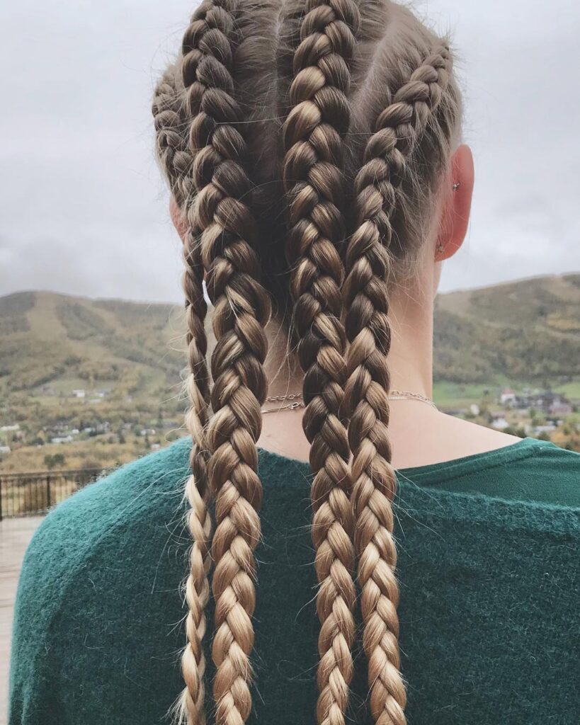 Back view of long multi braid sporty hairstyle with brunette and caramel tones.