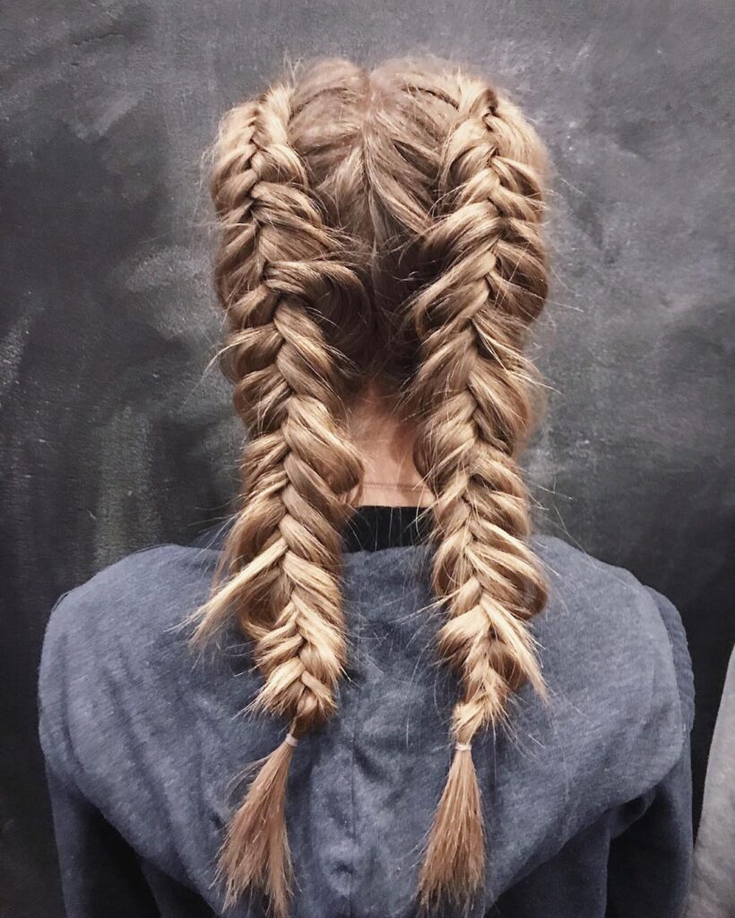 Back view of textured blonde boxer braids styled into two sporty plaits with soft volume.