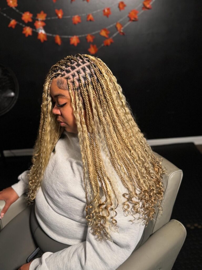 Blonde knotless braids with tight plaits at the roots and soft curly ends resting around the shoulders.