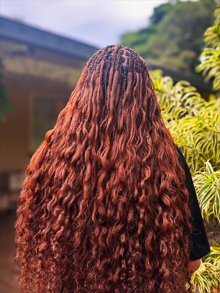 Long auburn knotless braids with loose voluminous wavy ends.