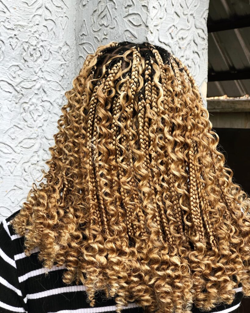 Golden blonde knotless braids with tight ringlet curls and full volume.