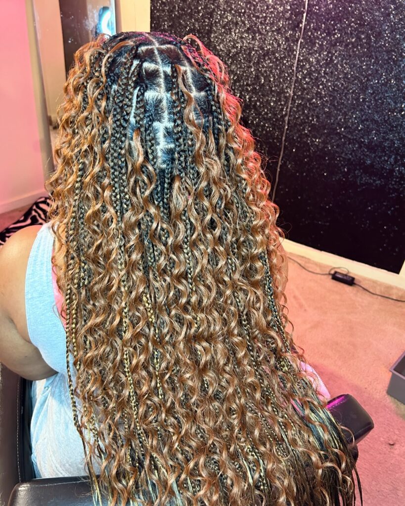 Honey blonde knotless braids with dark roots and defined curly texture.