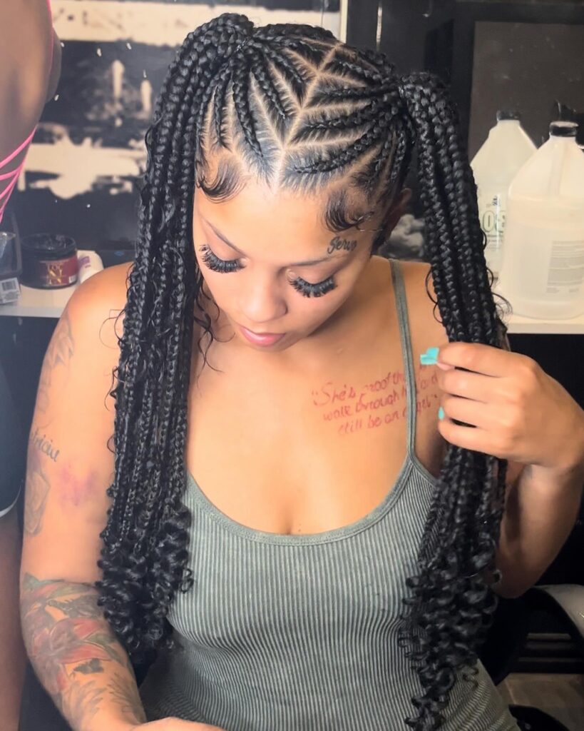 A woman with box braid ponytails styled with curled ends and detailed braid patterns.