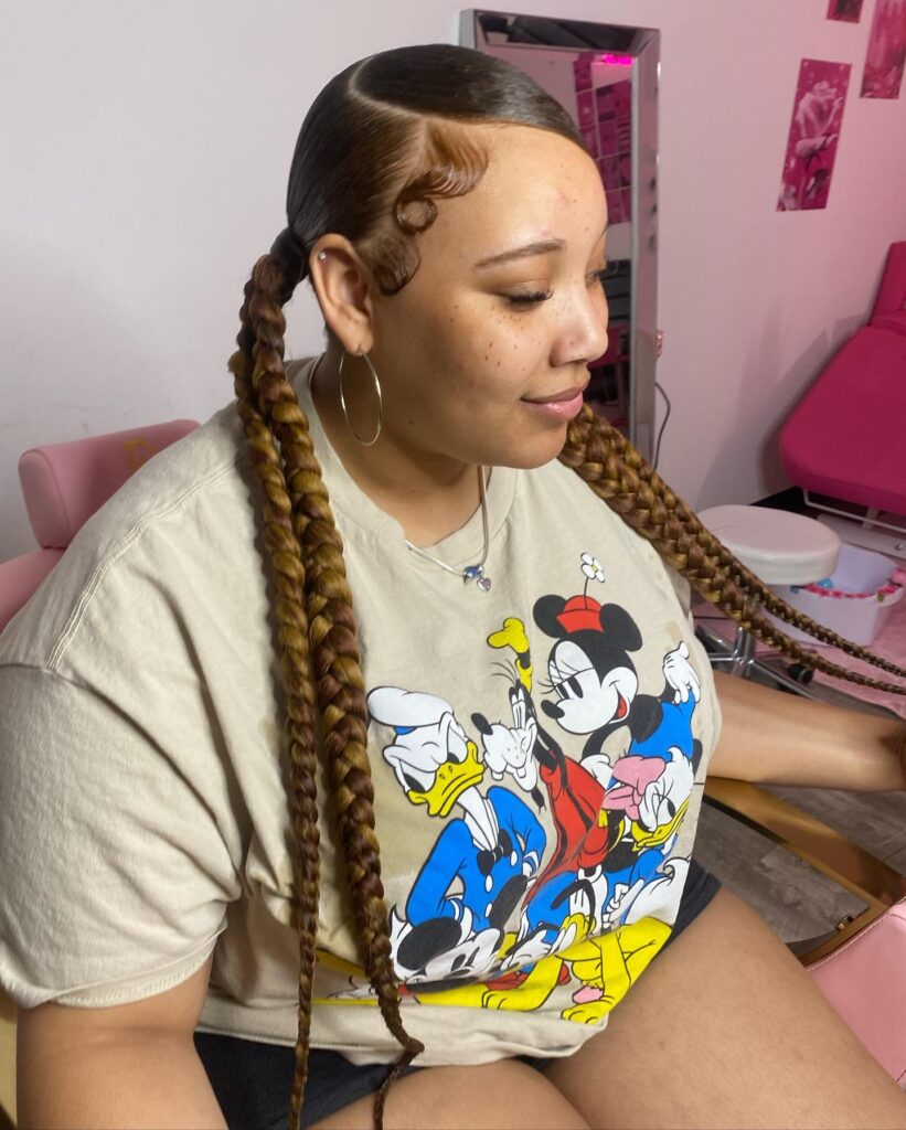 A woman with extra long honey blonde braided ponytails and sleek swooped edges.