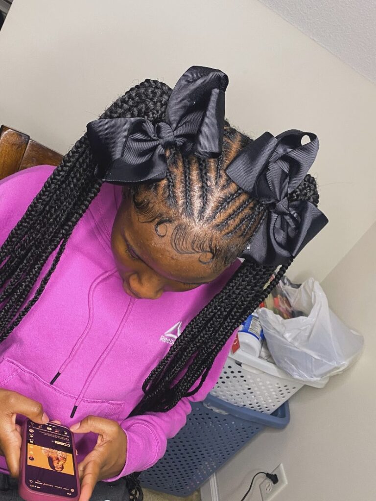 A woman with long braided ponytails styled with oversized black bows and neat cornrows.