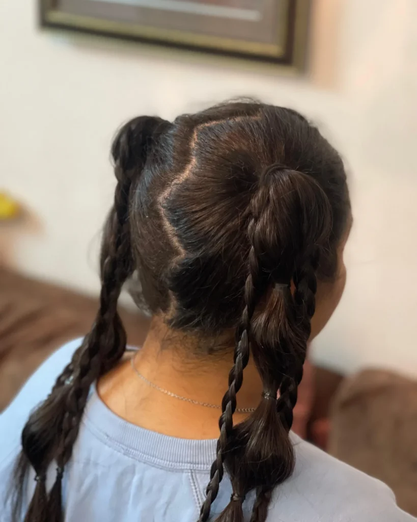 A young girl with two ponytails styled with twisted braid sections and zigzag parts.