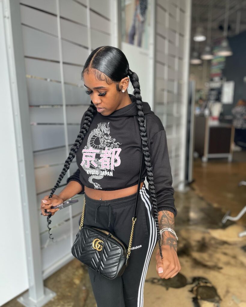 A woman wearing sleek extra long jumbo braided ponytails with a middle part and smooth laid edges.