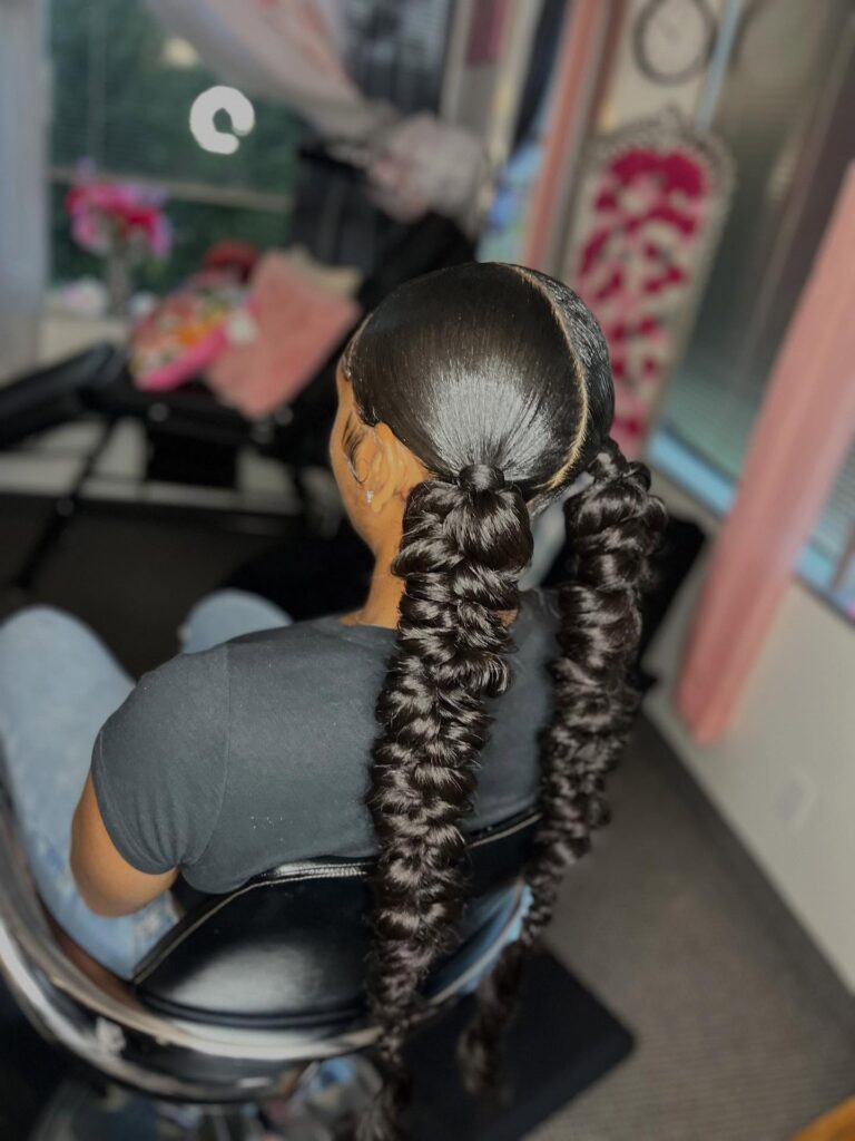 A woman wearing sleek two ponytails styled into long bubble twist sections with a middle part.