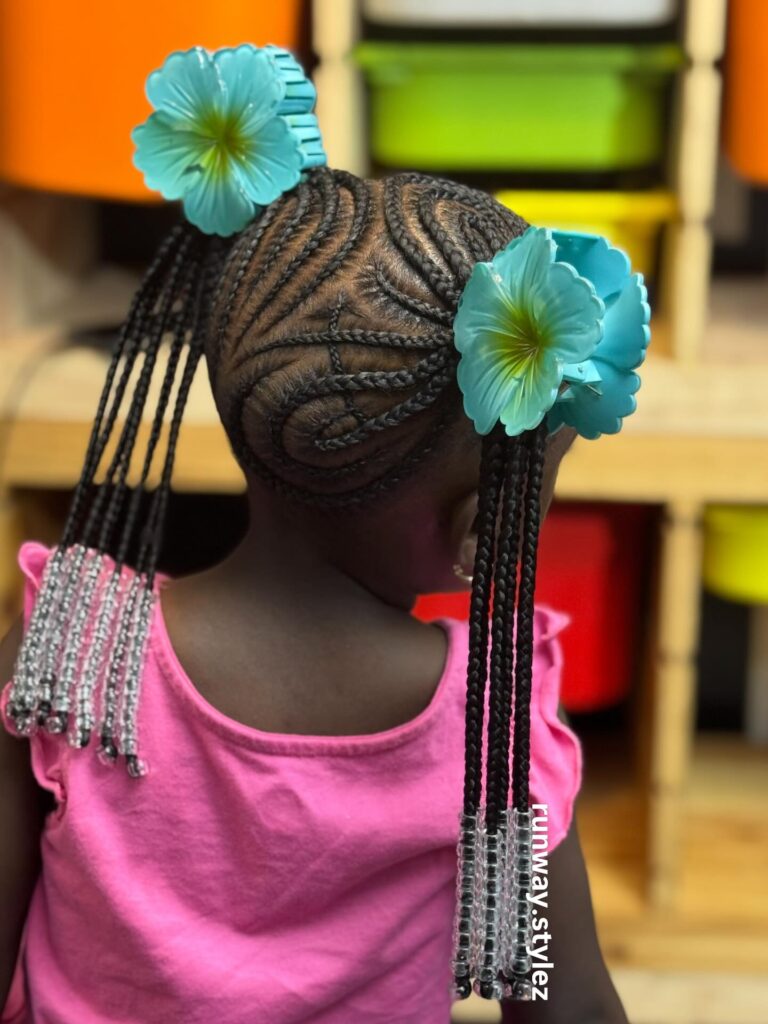 A young girl with braided ponytails featuring swirl braid patterns, beads, and blue flower clips.
