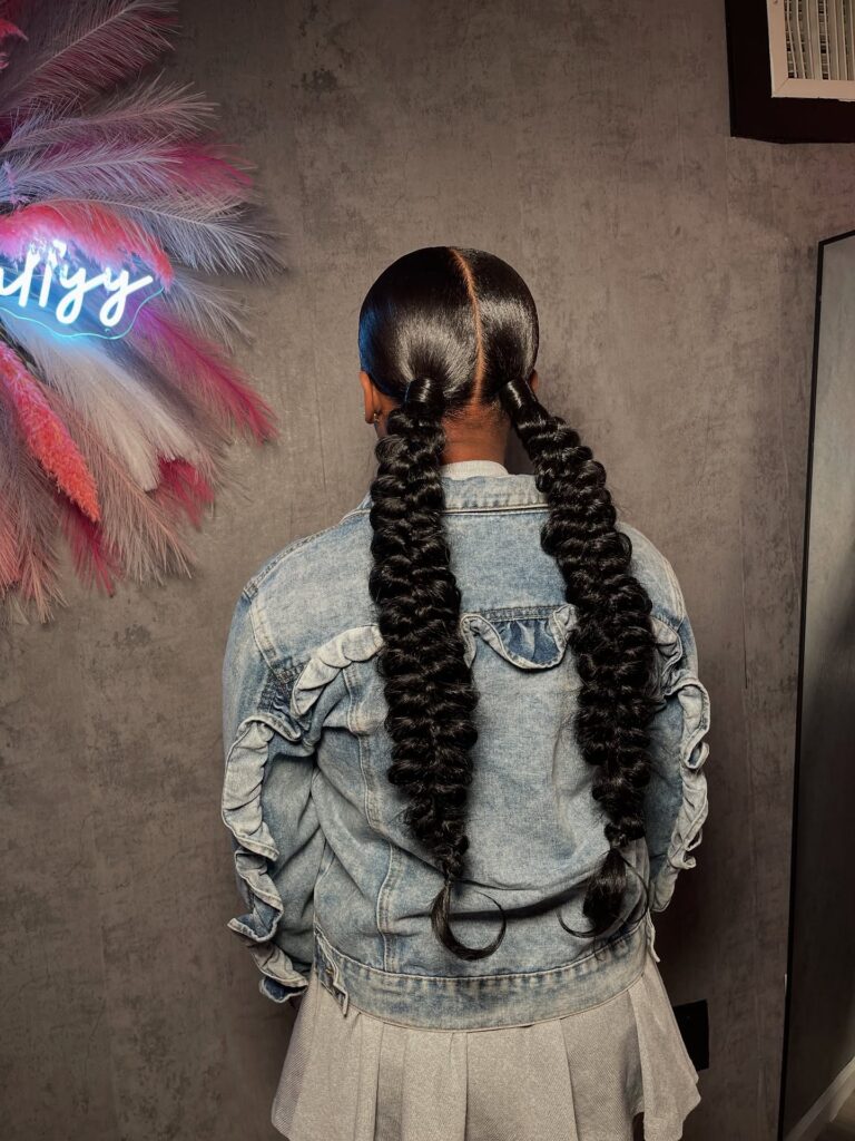 A woman with long spiral ponytails and sleek parted hair.