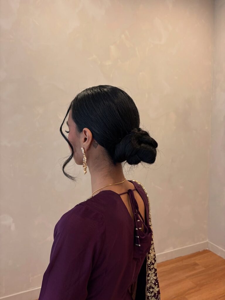 Sleek black braided low bun hairstyle with soft curled tendrils around the face.