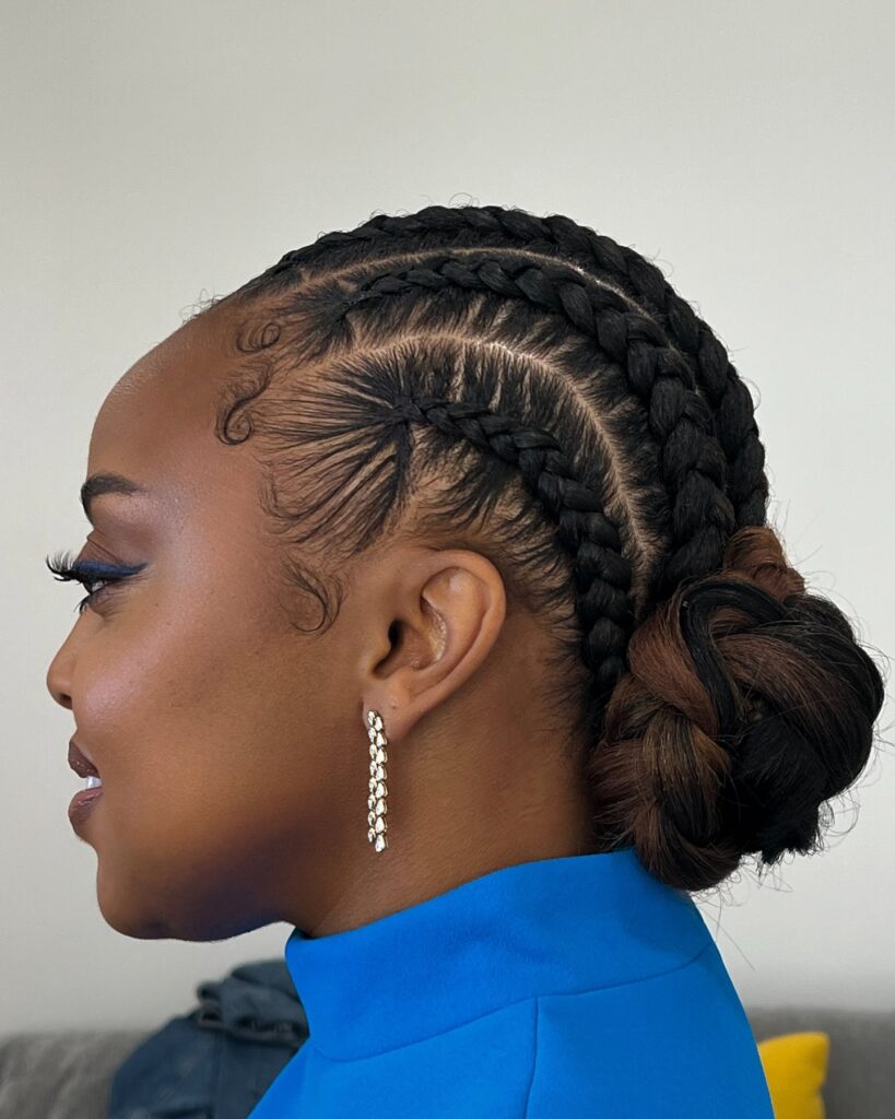 Low braided bun hairstyle with curved cornrows, swooped baby hairs, and brown toned bun details.