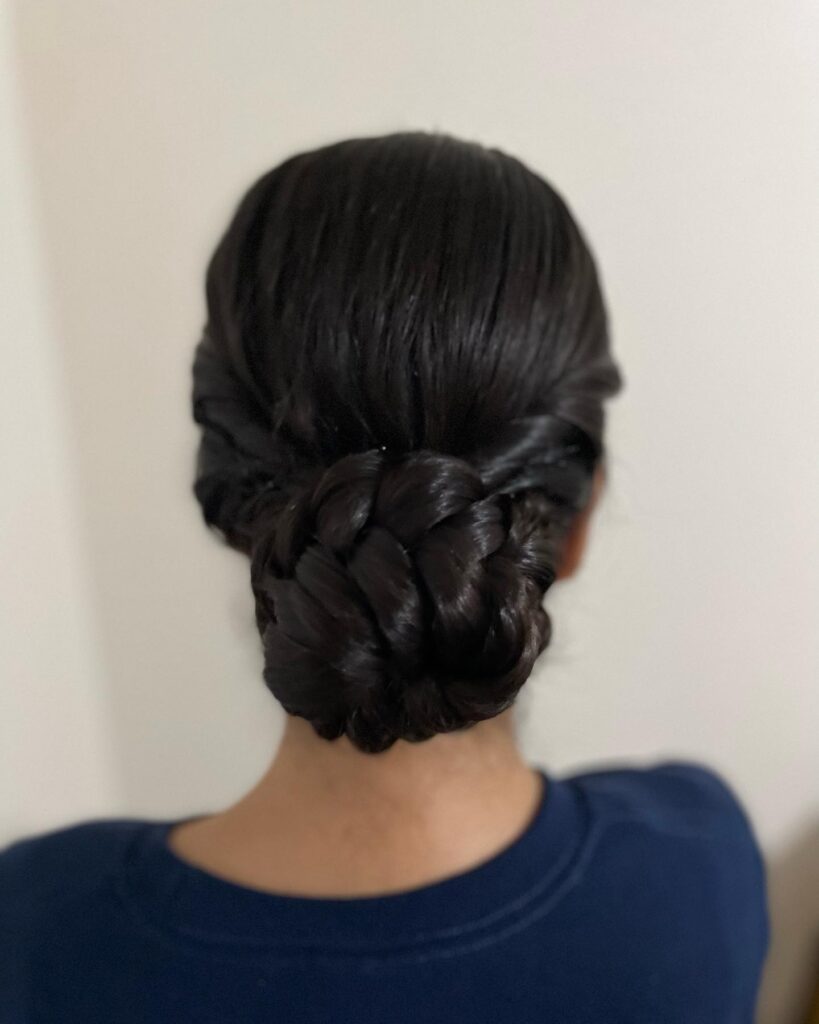 Sleek black low braided bun hairstyle with twisted sections and a smooth finish.